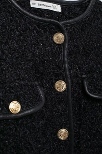 Détail de veste en tweed avec bordure en cuir noir et boutons dorés sur la poche