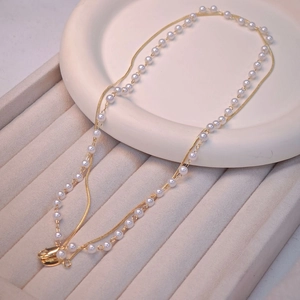 Double-layered gold chain and pearl necklace displayed on a beige jewelry tray