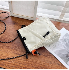 Detail of a minimalist cream canvas crossbody bag with contrast cord strap on a wooden desk