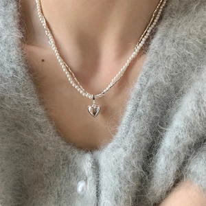 Dettaglio di una collana a due strati con perle e ciondolo a cuore in argento su modella