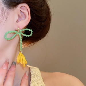 Dettaglio orecchino a fiore con fiocco di perline verdi e pendente a petalo giallo vivido
