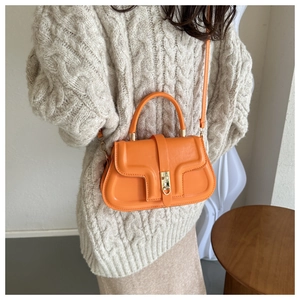 Detail of an orange saddle bag featuring a gold buckle on a beige knit sweater background