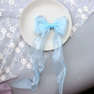 Macro shot of light blue sheer ribbon hair bow with long streamers on a lace background