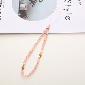 Pink beaded phone charm with crystal stones and golden clover detail on a desk