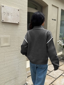 Outdoor shot of a grey knit sweater with high neck and white stripes on the shoulders