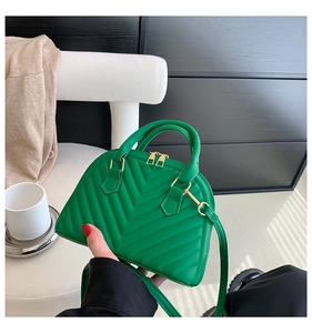 Detail of green V-quilted mini shell handbag with golden hardware being held