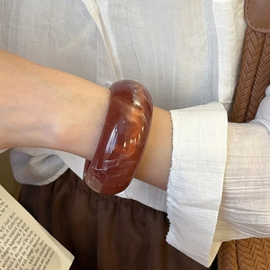 Detail of amber resin bangle with white marble texture on female wrist in soft light