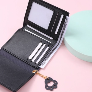 Detail of cute cat paw pendant on black textured faux leather trifold wallet interior