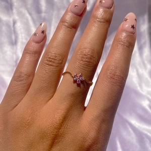 Detail of wavy gold beaded ring with iridescent flower pendant on purple silk fabric