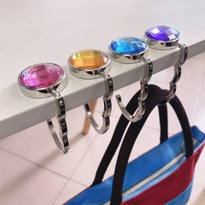 Portable round gemstone bag hooks in multiple colors hanging on a table edge