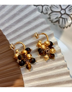 Detailed close-up of gold cluster earrings with brown tiger eye beads on a white backdrop