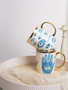 Close-up of ceramic mugs with blue evil eye patterns and gold handles on wooden tray