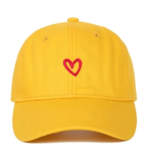Close-up of red heart embroidery on yellow cotton baseball cap with textured stitching