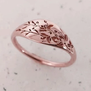 Detailed close-up of rose gold signet ring with intricate floral engraving on the top