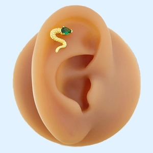Macro shot of gold snake cartilage earring with green zircon on realistic ear model