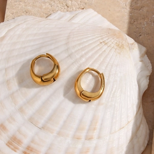 Macro view of gold plated pear shaped hoop earrings resting on a white seashell