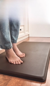 Close-up of bare feet on thick anti-fatigue PU leather kitchen mat with non-slip texture