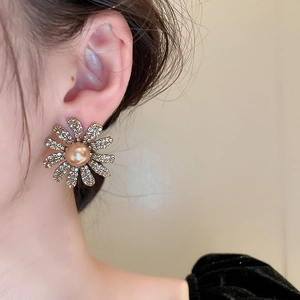 Close-up of golden daisy earring with sparkling crystals and bronze pearl on model