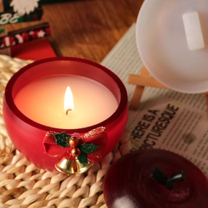 Bougie parfumée en forme de pomme de Noël avec nœud rouge et cloches dorées sur socle bois