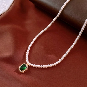 Detail of pearl necklace featuring rectangle green gemstone pendant with gold-plated setting