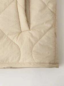 Detailed macro view of beige quilted fabric texture and stitching on casual jacket
