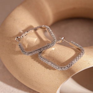 Detail shot of silver square geometric hoop earrings on a beige ceramic pedestal
