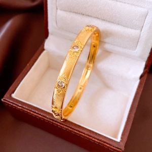 Detailed close-up of 24K gold plated bangle with starburst pattern and clear gemstones