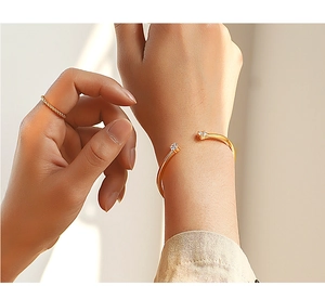 Close-up of minimalist gold open bangle with twin zircons and a twisted rope ring