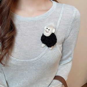 Detail of a handmade sheep brooch in black and white plush on a grey knit sweater