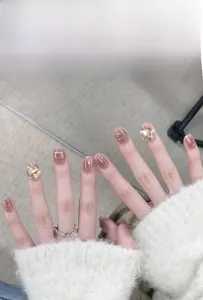 Détail macro de faux ongles dégradé rose nude avec papillon 3D et diamant en cristal