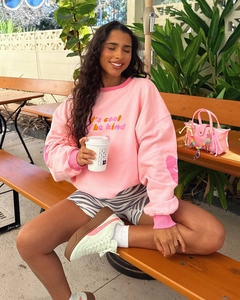 Detail of pink crewneck sweatshirt with 'it's cool to be kind' print and heart cuff