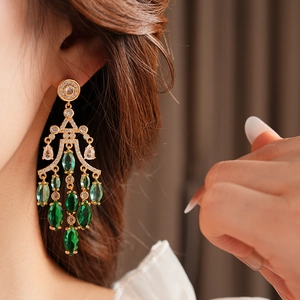 Detail of luxury gold drop earrings featuring green crystals and sparkling zircons