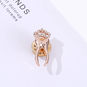 Rose gold dental tooth brooch with crown and white rhinestones on a white background