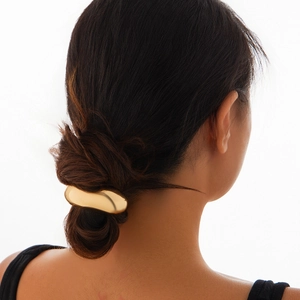 Minimalist gold metal curved hair accessory on a low bun hairstyle with back view