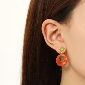 Detail of amber resin hoop earrings with hammered gold metal base on a female model