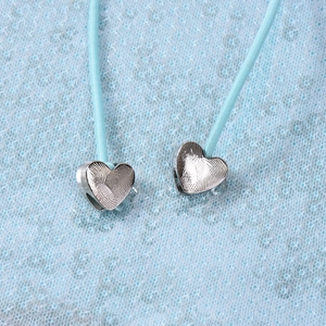 Gros plan de pendentifs cœur argentés texturés empreinte sur tissu à paillettes bleu clair