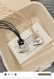 Dettaglio di ciondoli minimalisti a forma di borsa su cordini intrecciati neri e beige