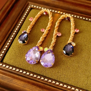 Macro detail of vintage gold woven earrings with purple teardrop gemstone on green velvet