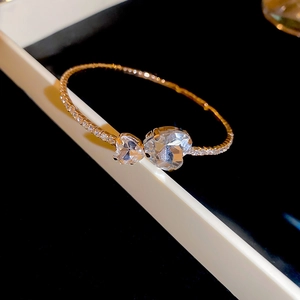 Macro detail of gold-plated open bangle featuring dual heart crystals and pave setting
