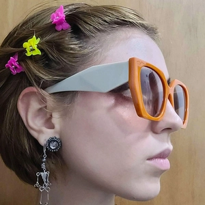 Detail of vibrant orange square sunglasses with butterfly clips and wire drop earring