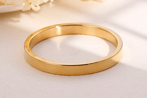 Minimalist gold stainless steel ring displayed on warm neutral background with dried flowers