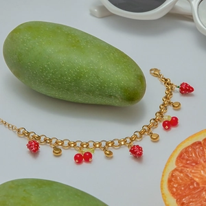 Detail view of a gold chain bracelet with red strawberry and cherry enamel pendants