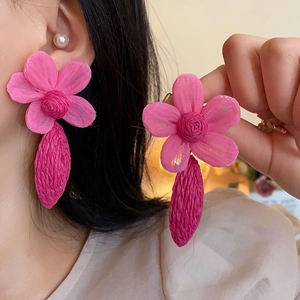 Close-up of pink fabric flower earrings with tassel pendant on model's ear