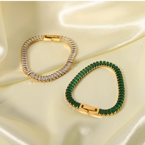Detail of gold-plated bracelets with emerald green and clear zircon stones on silk fabric