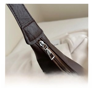 Close-up of smooth silver metal zipper and brown leather texture on a tote bag