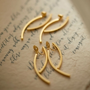 Elegant gold minimalist long drop clip-on earrings displayed on vintage paper backdrop