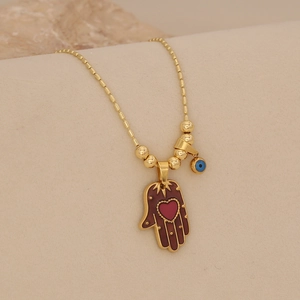 Detailed view of golden Hamsa hand pendant with red heart and blue evil eye bead on chain