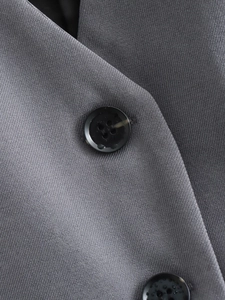Gros plan sur la texture du tissu sergé gris foncé et le bouton noir à quatre trous du gilet