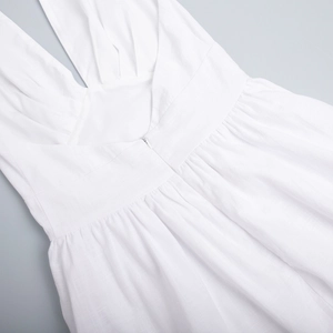 Detail of white cotton dress featuring deep V-neck, waist pleats, and invisible zipper
