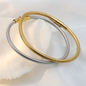 Detail of elegant gold and silver snake bone bracelets on a textured white fabric surface